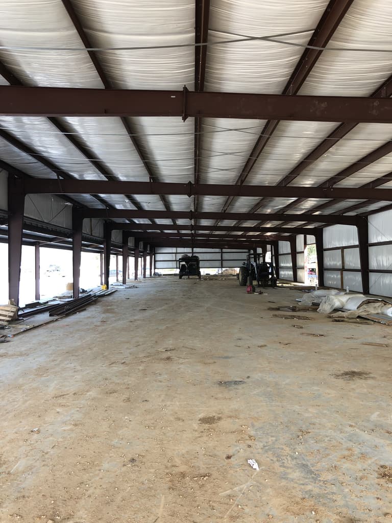 Long clear-span steel equipment barn interior with red-iron frames, insulated roof and a tractor parked inside