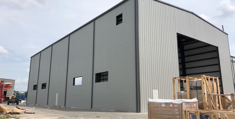 Finished gray steel warehouse with vertical wall panels, framed window openings and a large drive-in door on the endwall