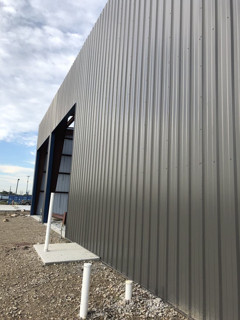 Close view of gray PBR steel wall panels on a new building with blue-framed door openings