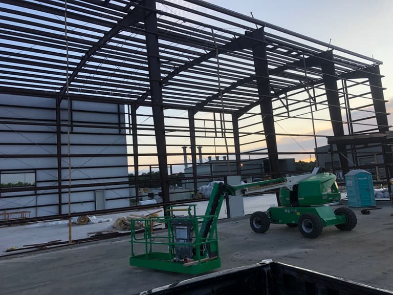 Steel building frame at dusk with a green boom lift on the slab during erection